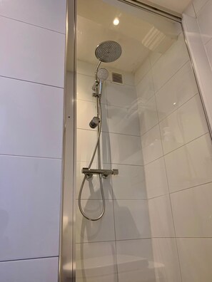 Une douche à l’italienne avec des parois en verre, dotée d’un pommeau de douche à main et d’une douchette à pluie fixée au mur.