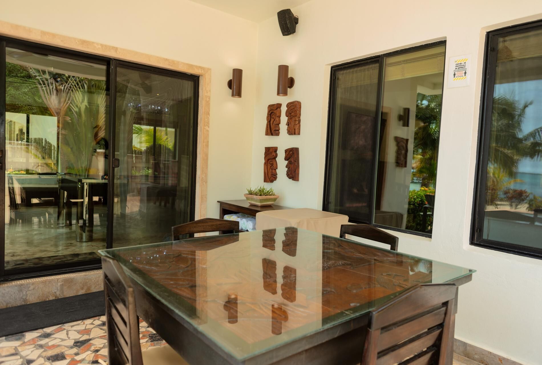 Comedor con mesa de vidrio, sillas y vista al exterior a través de amplias ventanas.
