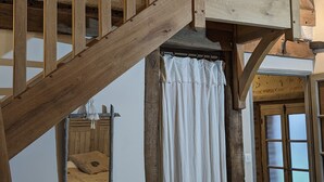 Una escalera de madera rústica que conduce a un nivel superior, una pequeña mesa con una silla y un ventanal con vistas al exterior.