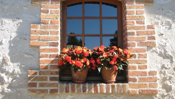 Una ventana con un arco de ladrillo y dos macetas de terracota con flores rojas.