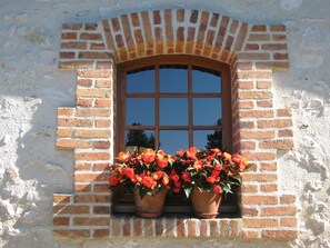 Una ventana con un arco de ladrillo y dos macetas de terracota con flores rojas.