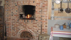 Una chimenea de ladrillo con fuego, un taburete de madera y una mesa con diversos utensilios de cocina.