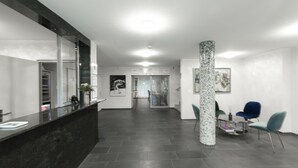 A modern reception area with a dark marble counter, a glass-top table with chairs, and a tiled floor. - Hotel Birsighof (Basel)