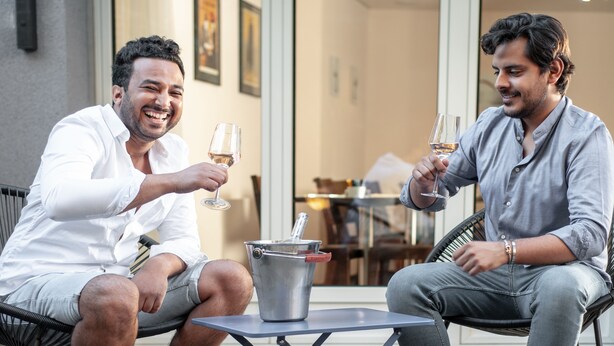 Two men seated on wicker chairs, holding wine glasses, with a metal bucket between them. - Hotel Birsighof (Basel)