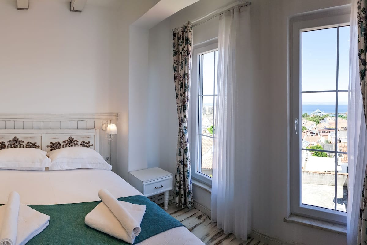 A hotel room with a bed, a nightstand, a window with curtains, and an air conditioning unit.