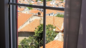 A view through a window of a coastal town with a historic fort, terracotta-roofed buildings, and a clear blue sky. - Bozcaada FRESH HOTEL (Bozcaada)