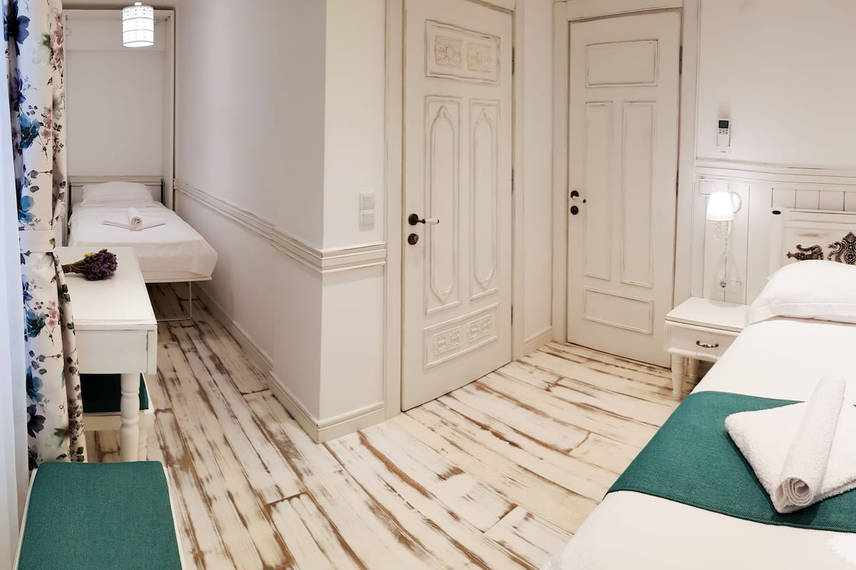 A hotel room with a bed, a bedside table, a nightstand, a mirror, a wardrobe, and a bathroom with a toilet and sink.