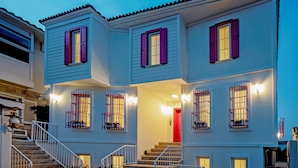 A two-story building with a red door, multiple windows with shutters, and a staircase leading to the entrance. - Bozcaada FRESH HOTEL (Bozcaada)