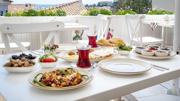 A dining table set outdoors with various dishes, a red cup, and white chairs. - Bozcaada FRESH HOTEL (Bozcaada)