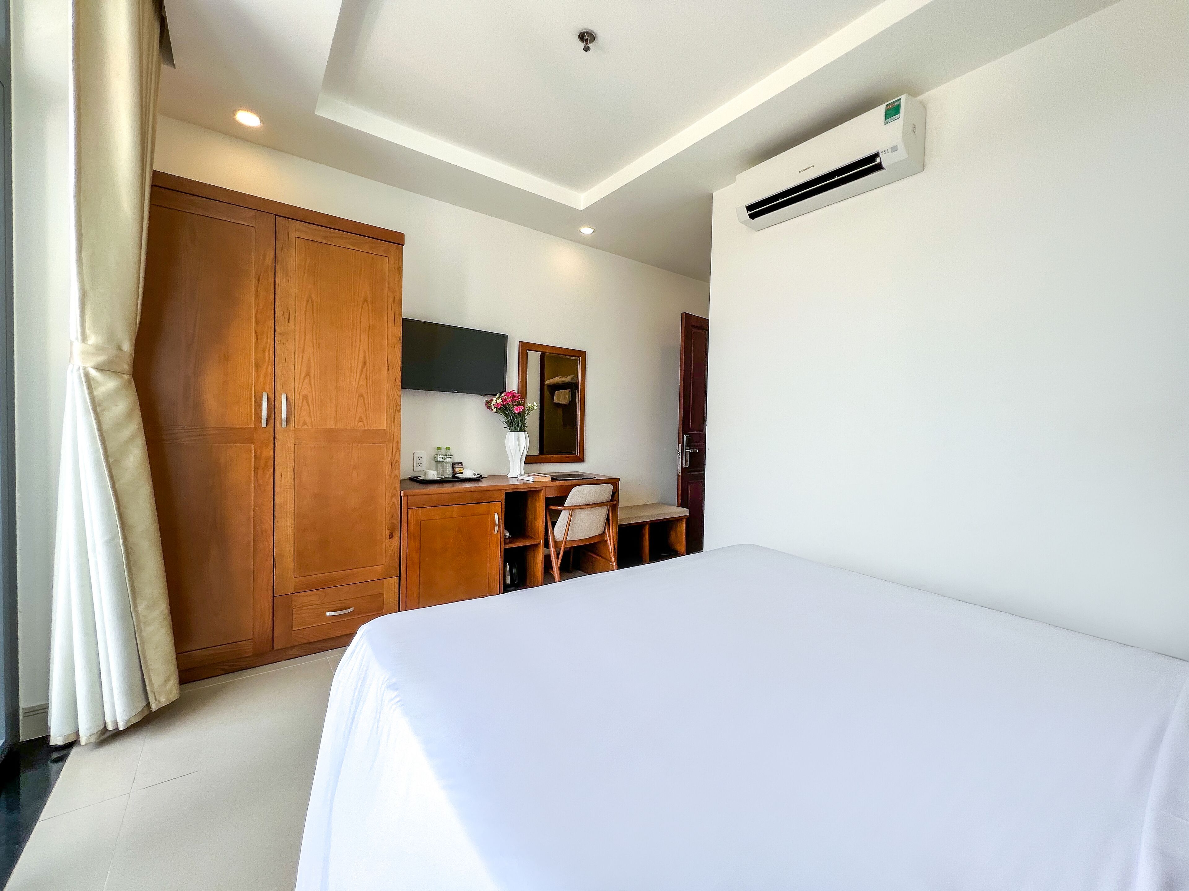 A hotel room with a bed, a desk with a chair, a wardrobe, a flat-screen TV, and an air conditioning unit.