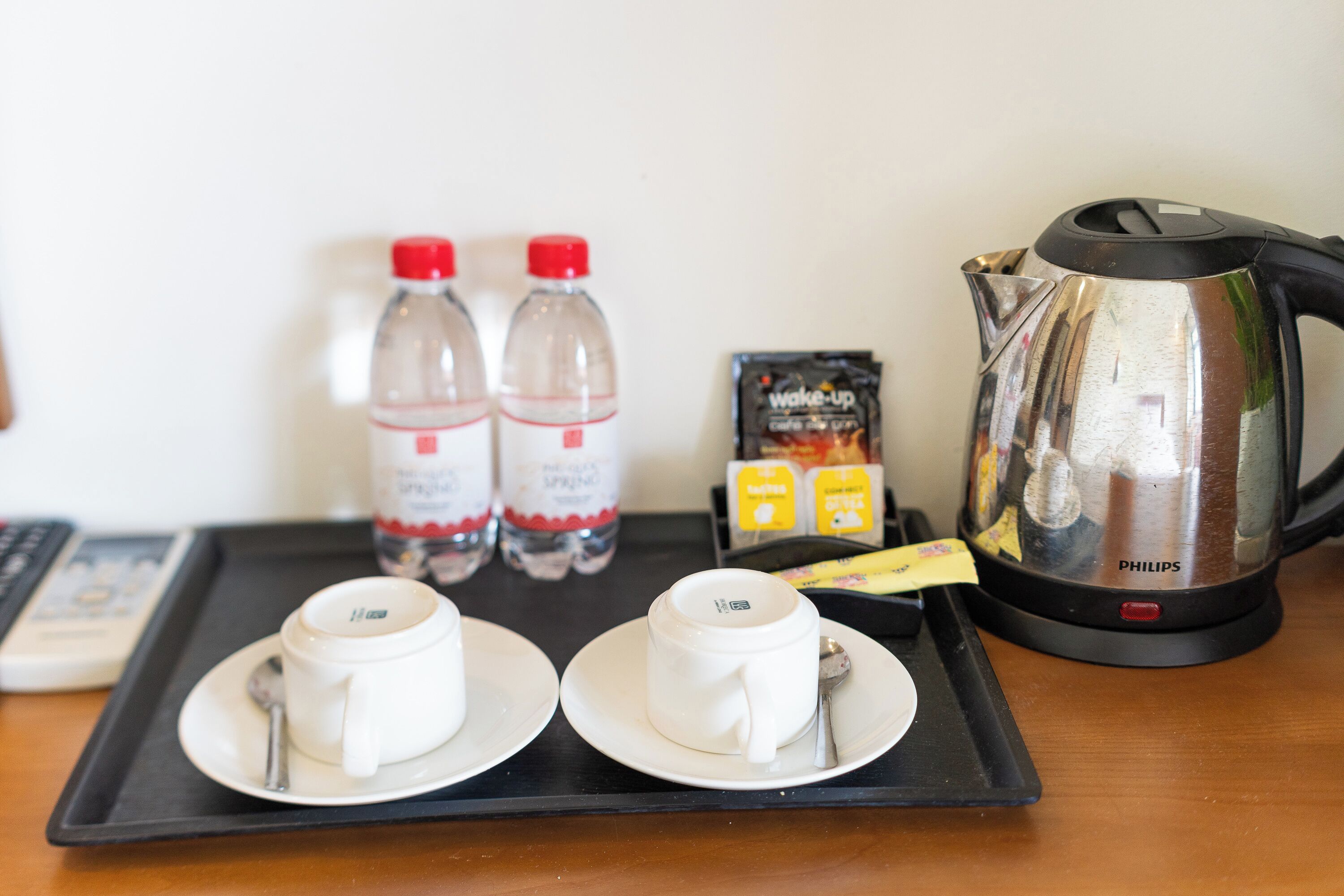 A tray with two cups, two bottles of water, a coffee maker, and a box of instant coffee.