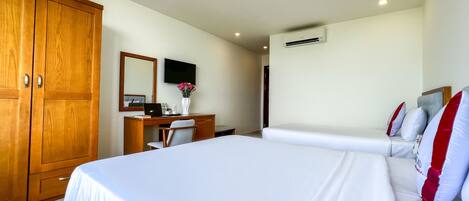A hotel room with a large bed, a desk with a computer, a chair, a TV, and an air conditioning unit.