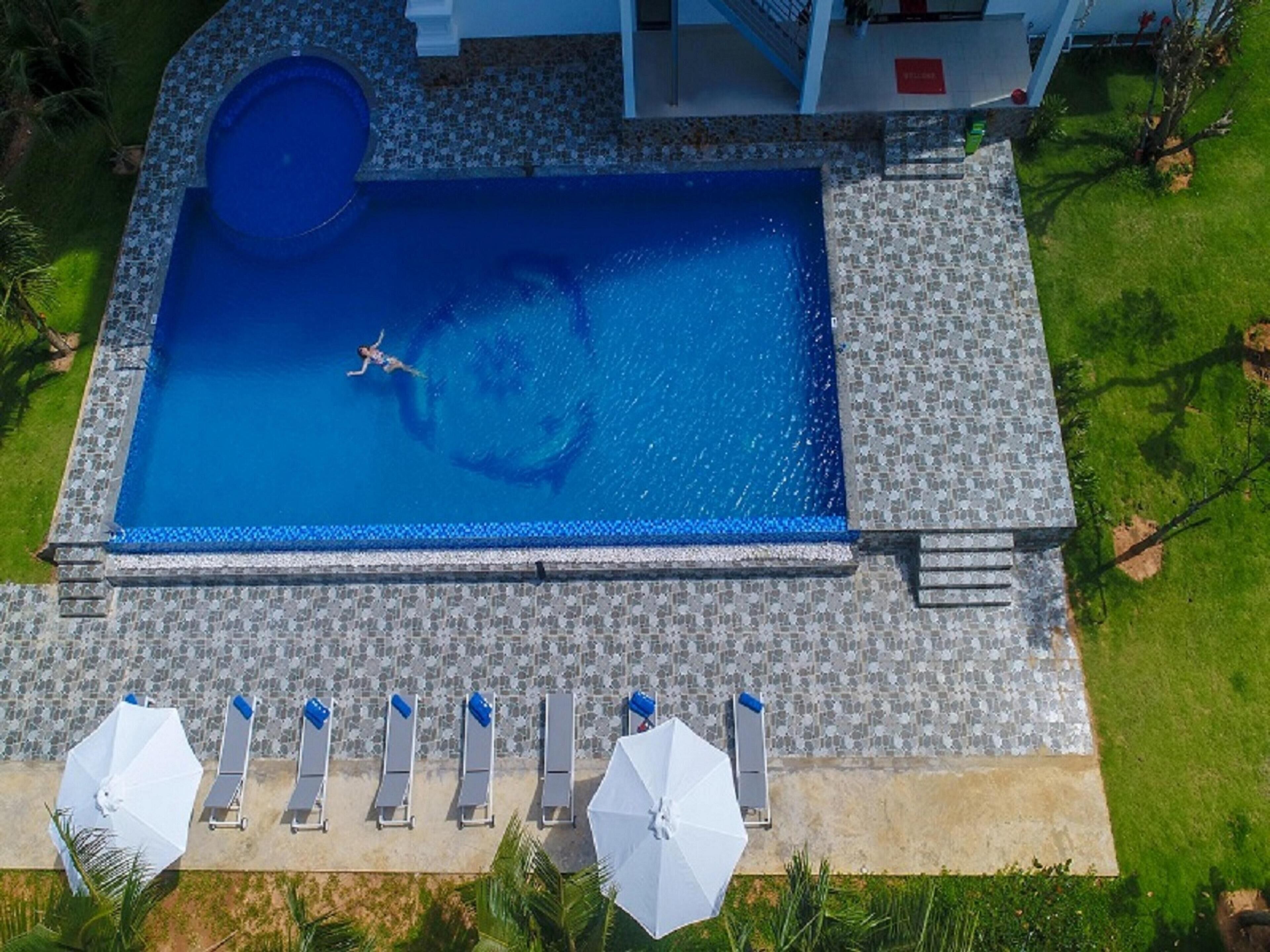 Una piscina rectangular con solárium empedrado, rodeada de sillones de descanso y sombrillas.