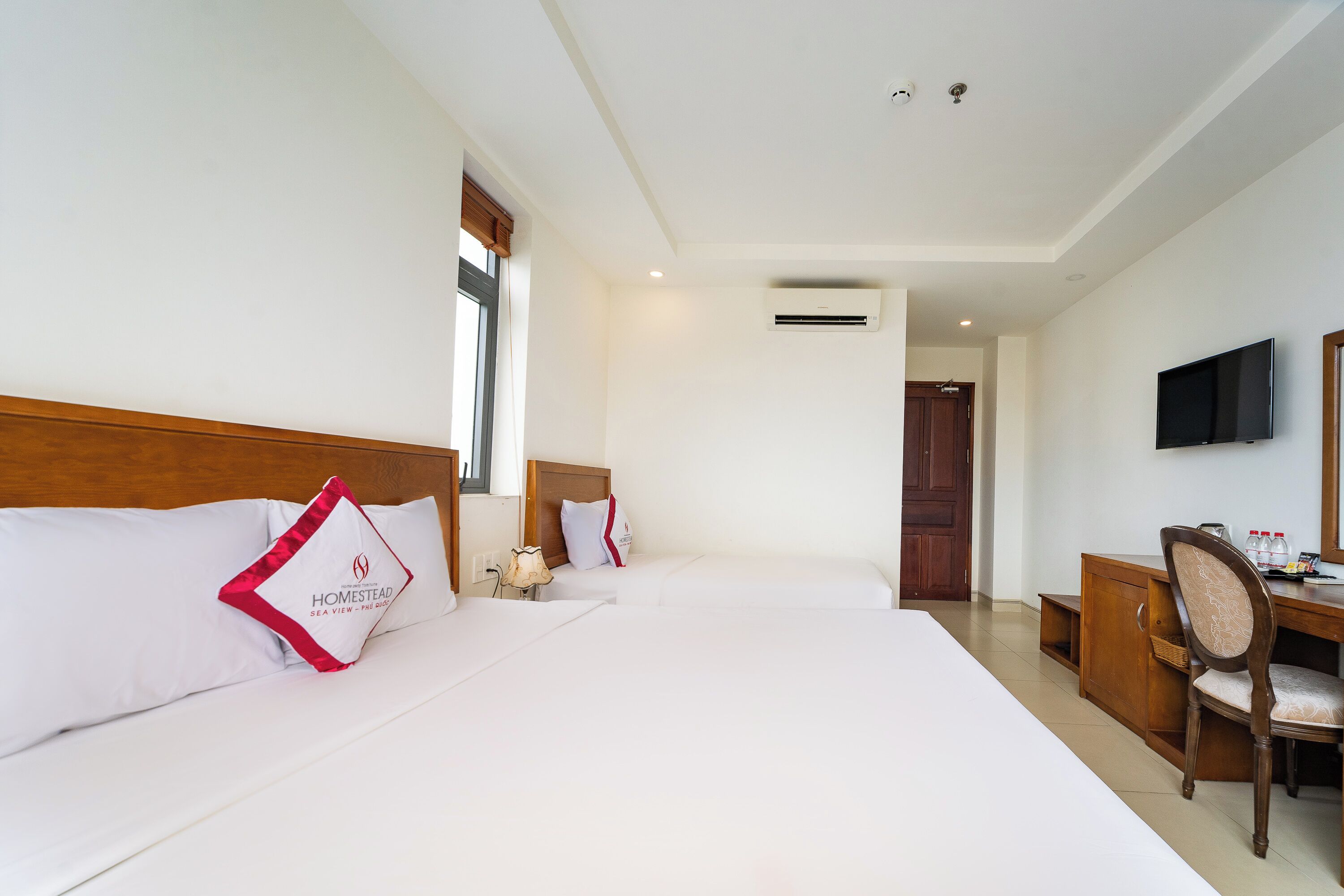Een hotelkamer met twee bedden, een bureau, een stoel, een televisie en een airconditioning.