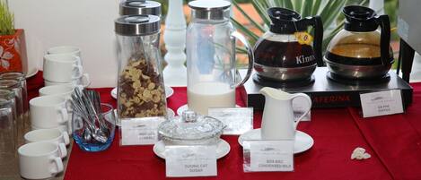 Een ontbijtbuffet met diverse etens- en drinkwaren, waaronder koffie en gecondenseerde melk.