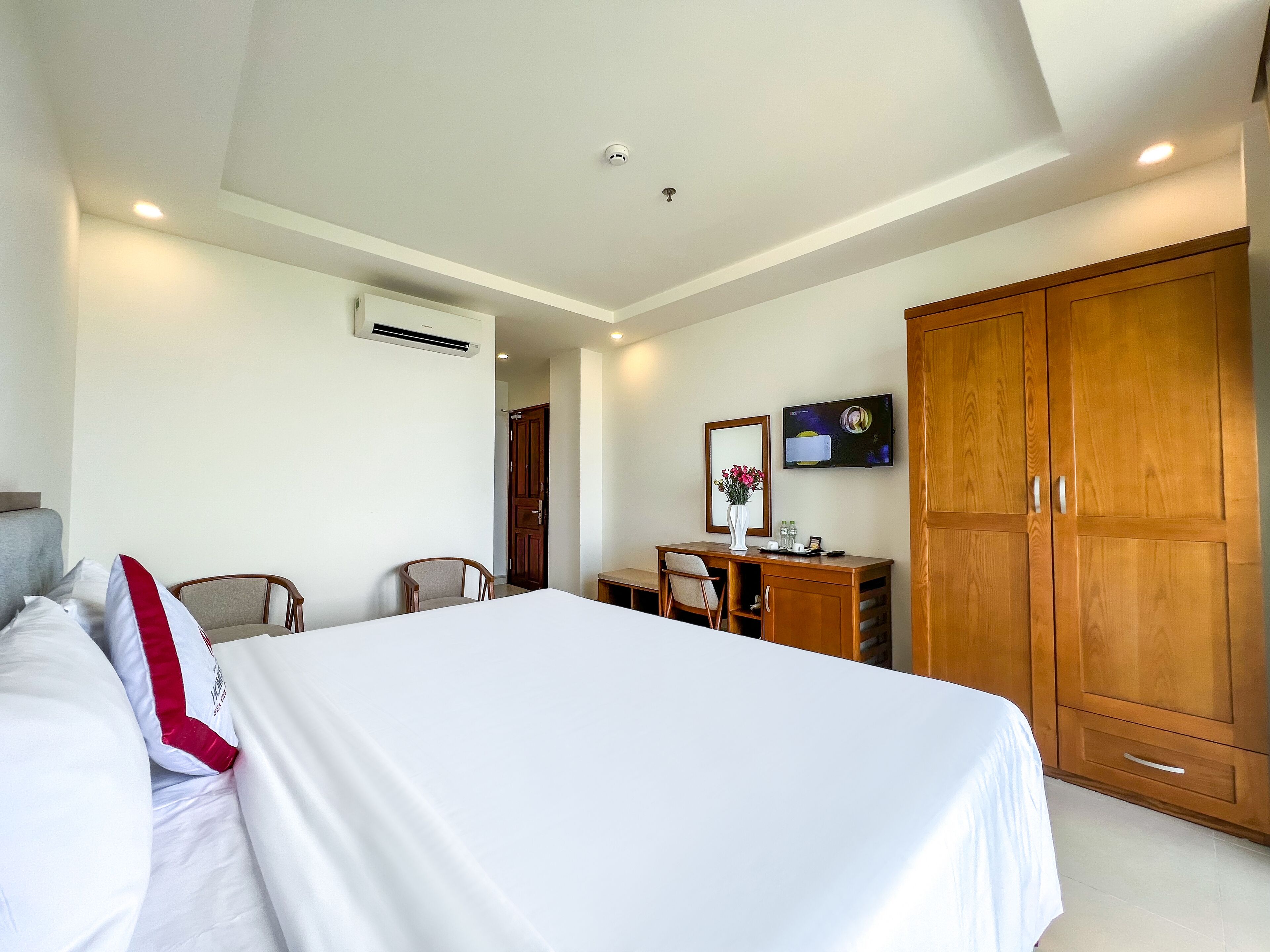 Habitación de hotel con cama, escritorio, silla, armario y televisión en la pared.