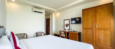 Habitación de hotel con cama, escritorio, silla, armario y televisión en la pared.