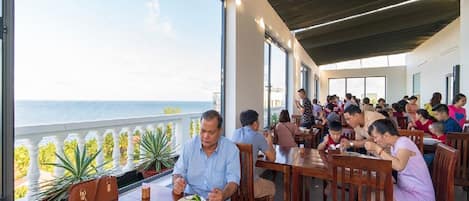 Un restaurante con amplios ventanales con vistas al mar, mesas y sillas de madera.