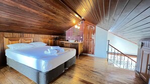 Un dormitorio con techo de madera, una cama, un baño con lavamanos y una escalera.