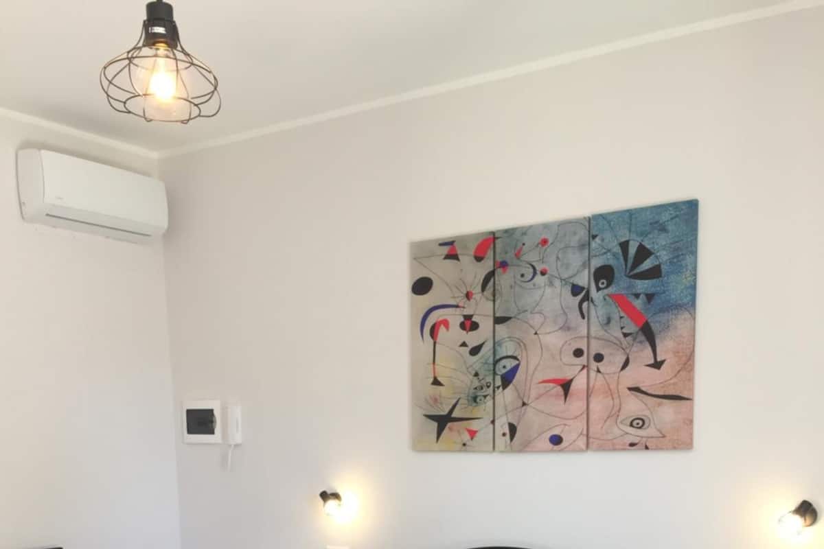 Une chambre à coucher comprenant un lit, deux tables de chevet, une chaise, un appareil de climatisation et une œuvre d’art accrochée au mur.