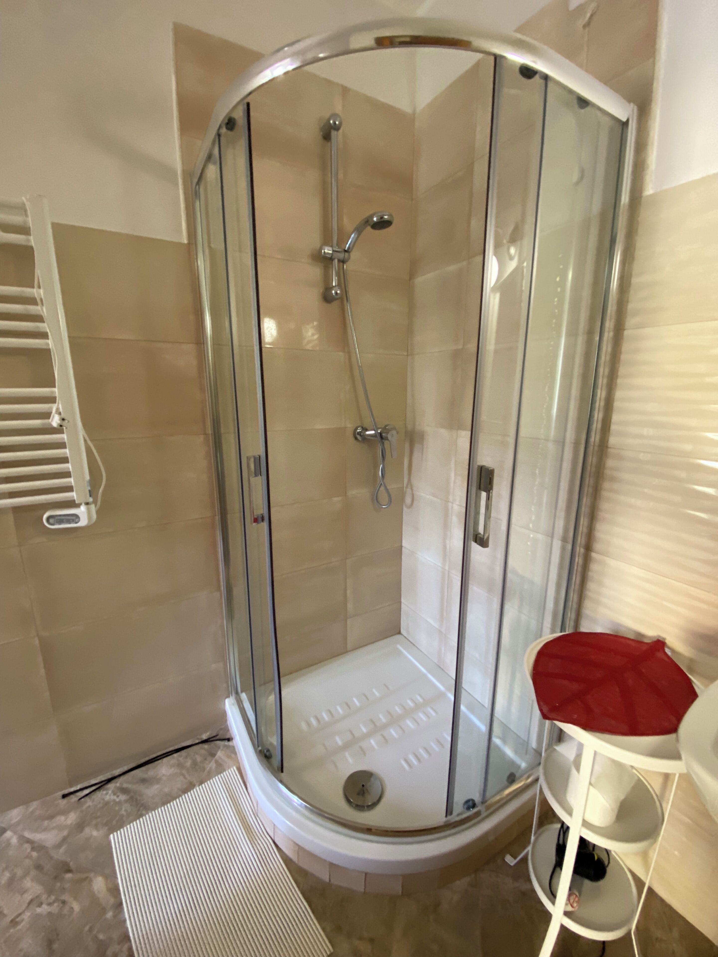 A glass-enclosed shower with a white floor, a white towel rack, and a white chair with a red cushion.