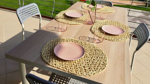 An outdoor dining area with a wooden table set for four, surrounded by metal chairs.