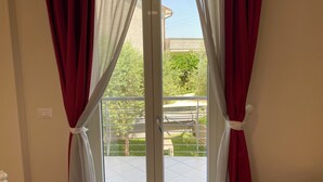 A room with a sliding glass door leading to an outdoor area with a metal railing and greenery.