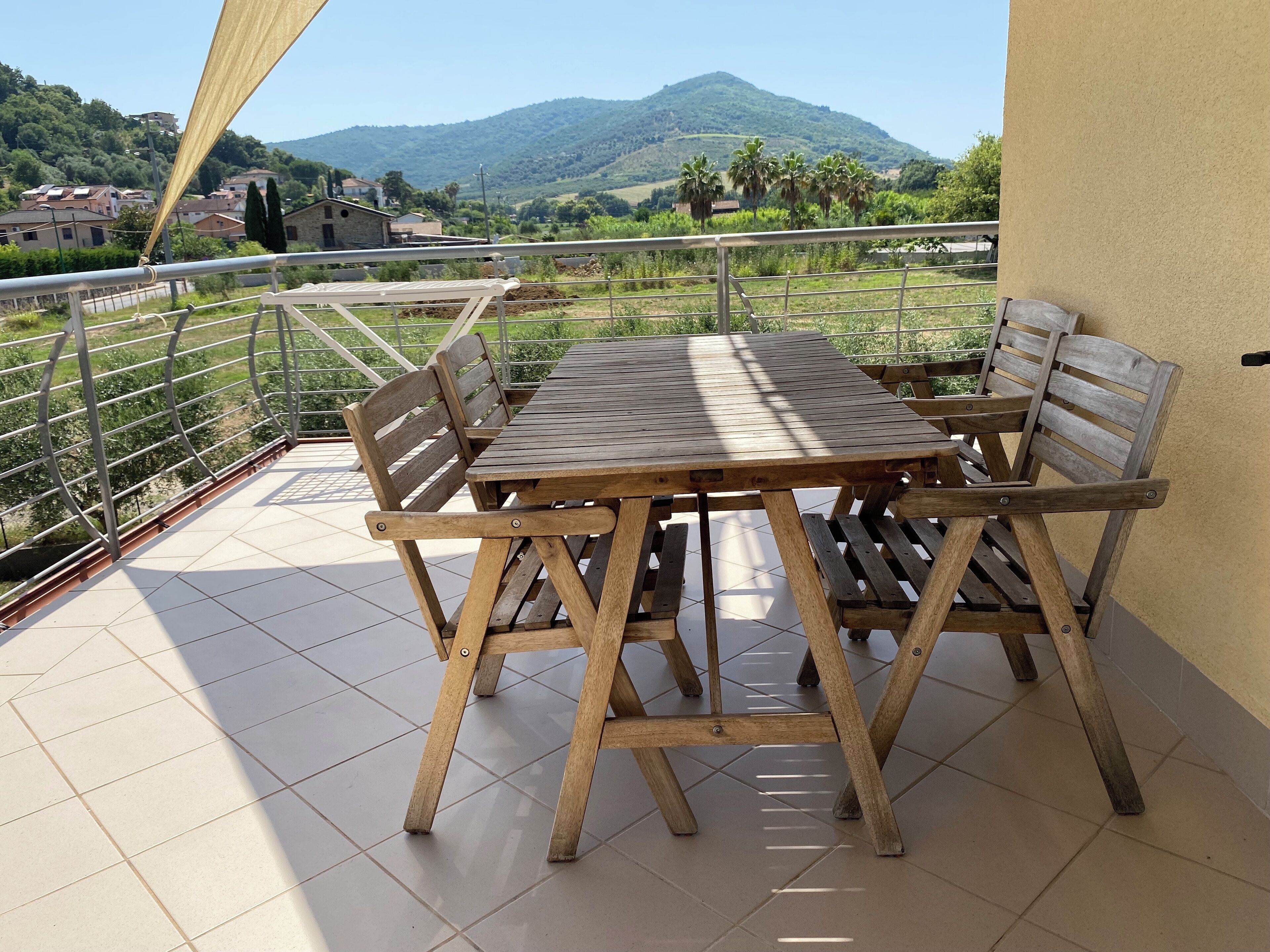A wooden table and chairs on a balcony with a view of a mountain and houses in the background.