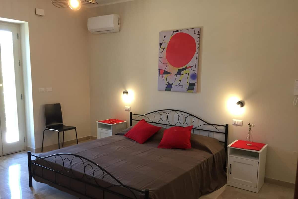 Une chambre à coucher comprenant un lit, deux tables de chevet, une chaise, un climatiseur fixé au mur et un tableau.