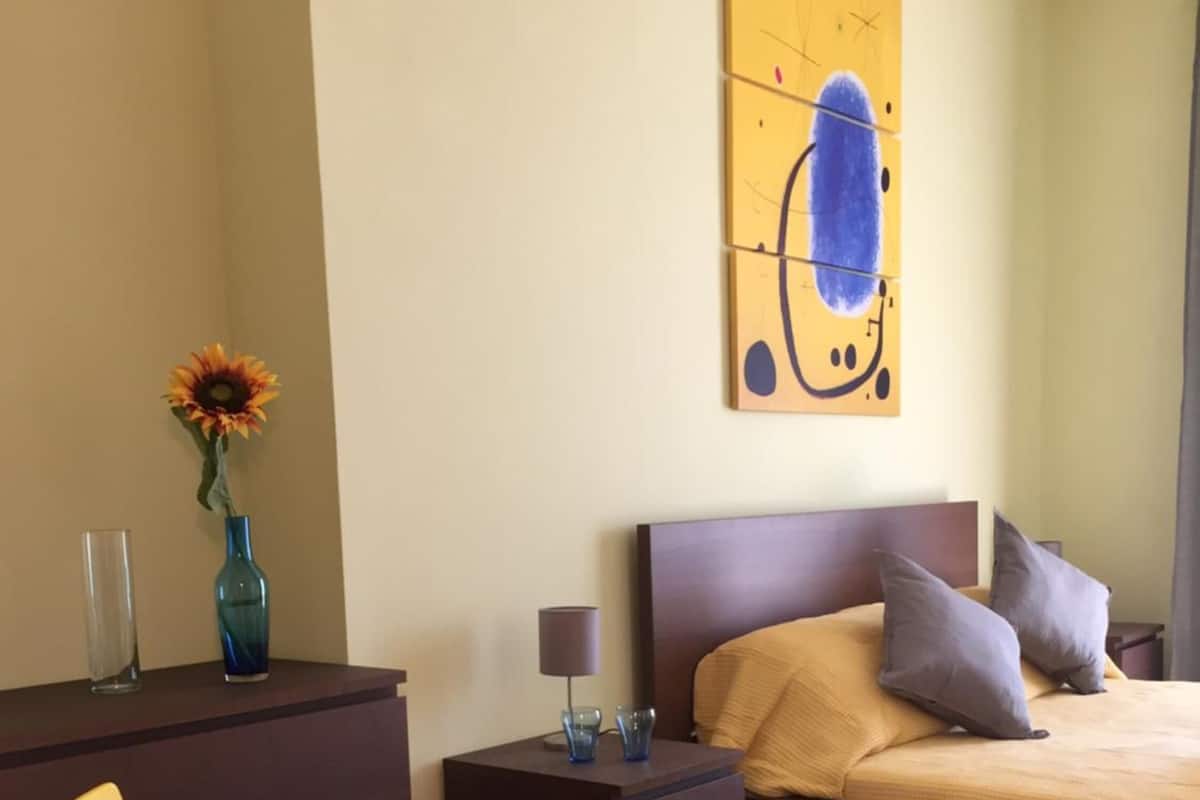 Une chambre à coucher comprenant un lit, des tables de chevet, une commode, une chaise et un tableau accroché au mur.