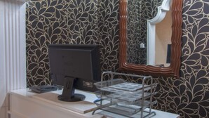 Een kamer met behang met een patroon, een bureau met een computer en een metalen dienblad, en een spiegel met een sierlijk lijstwerk.