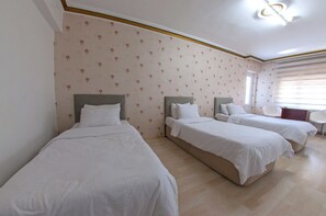 Habitación de hotel con tres camas individuales, una mesita y una ventana con persianas.