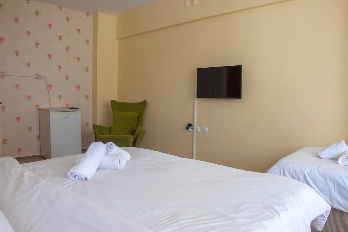 A hotel room with two beds, a green chair, a TV on the wall, and a small desk with a power outlet.