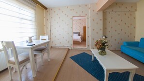 Een kamer met een eettafel, stoelen, een blauwe bank en een bed op de achtergrond.