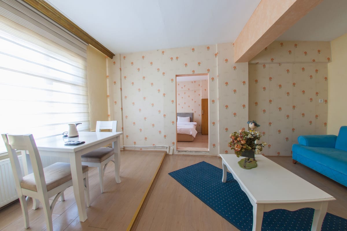 A room with a dining table, chairs, a blue sofa, and a bed in the background.