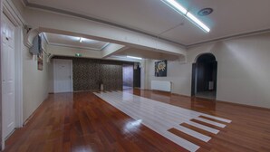 Een ruime hal met houten vloeren, witte muren en een plafond met fluorescentie verlichting.