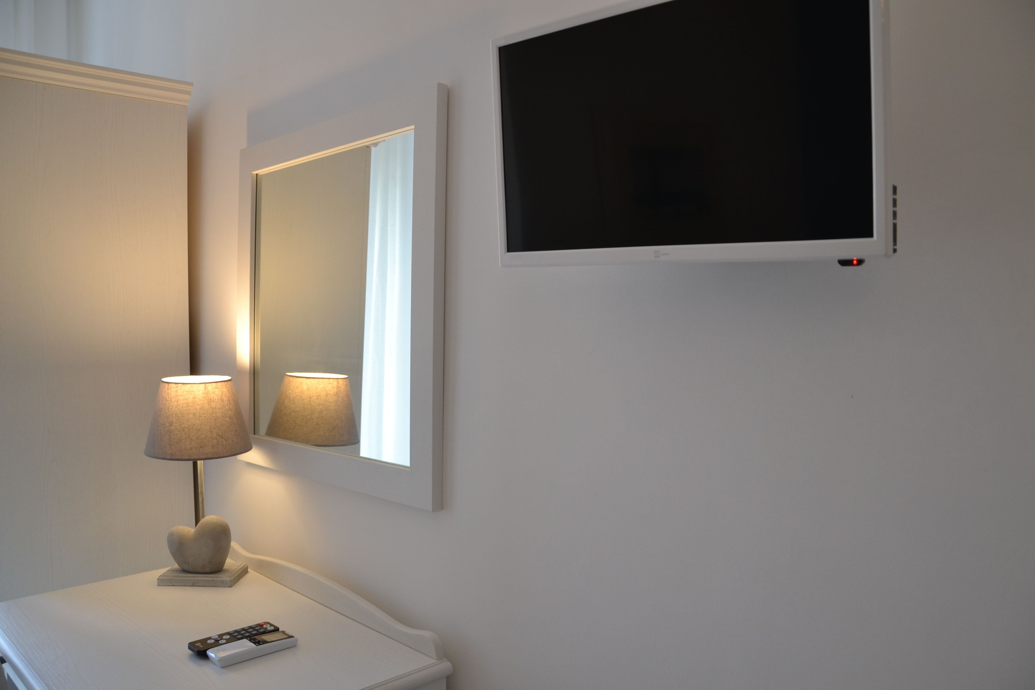 Un comodino bianco con un telecomando, una lampada e uno specchio.