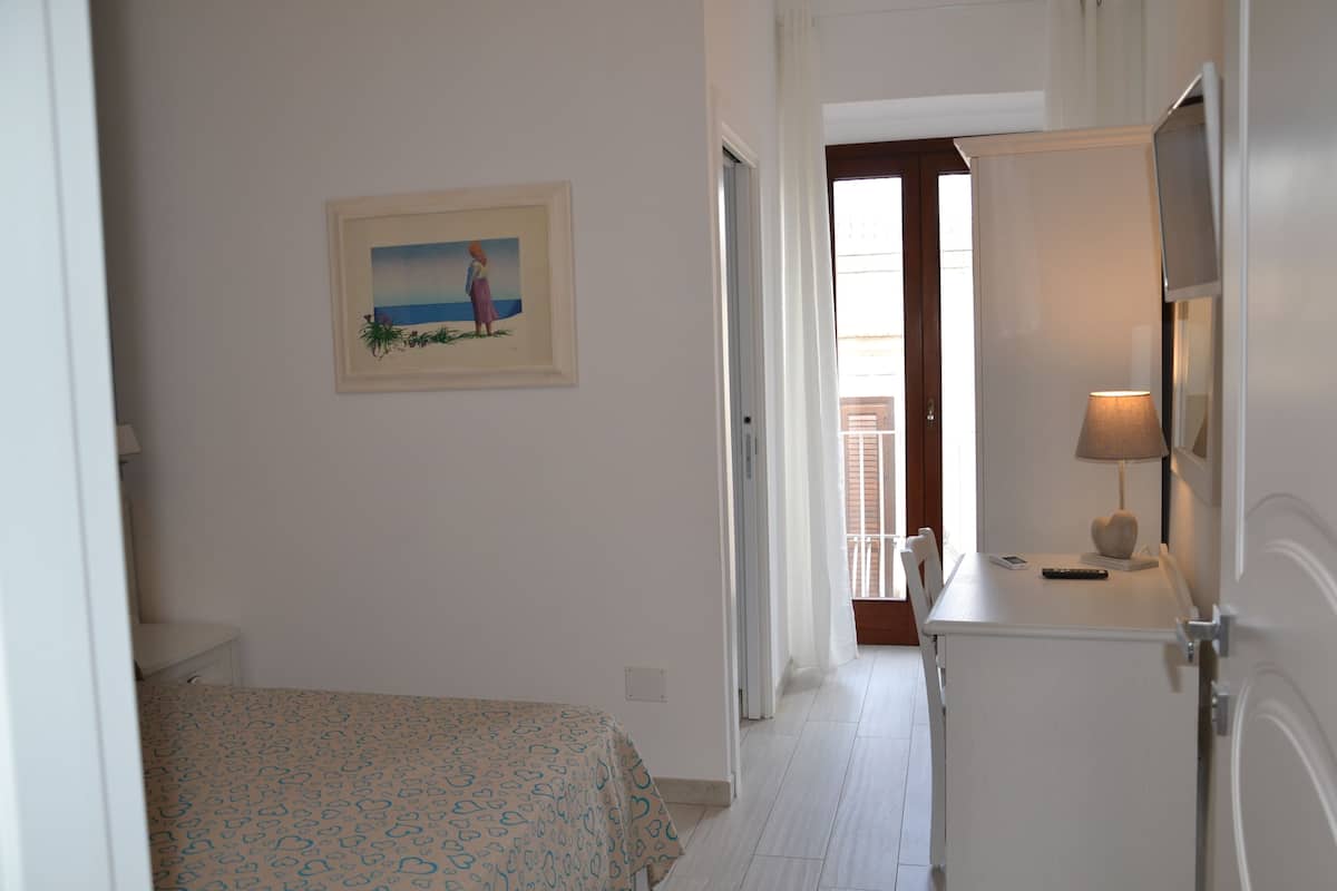 A bedroom with a bed, a desk, a chair, a lamp, and a painting on the wall.