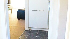 En hall med en vit dörr, mörkt kakelgolv och en blå soffa i bakgrunden.