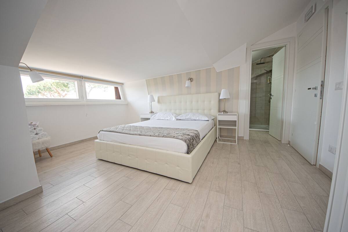A bedroom with a bed, bedside tables, a window, and a door leading to a bathroom.