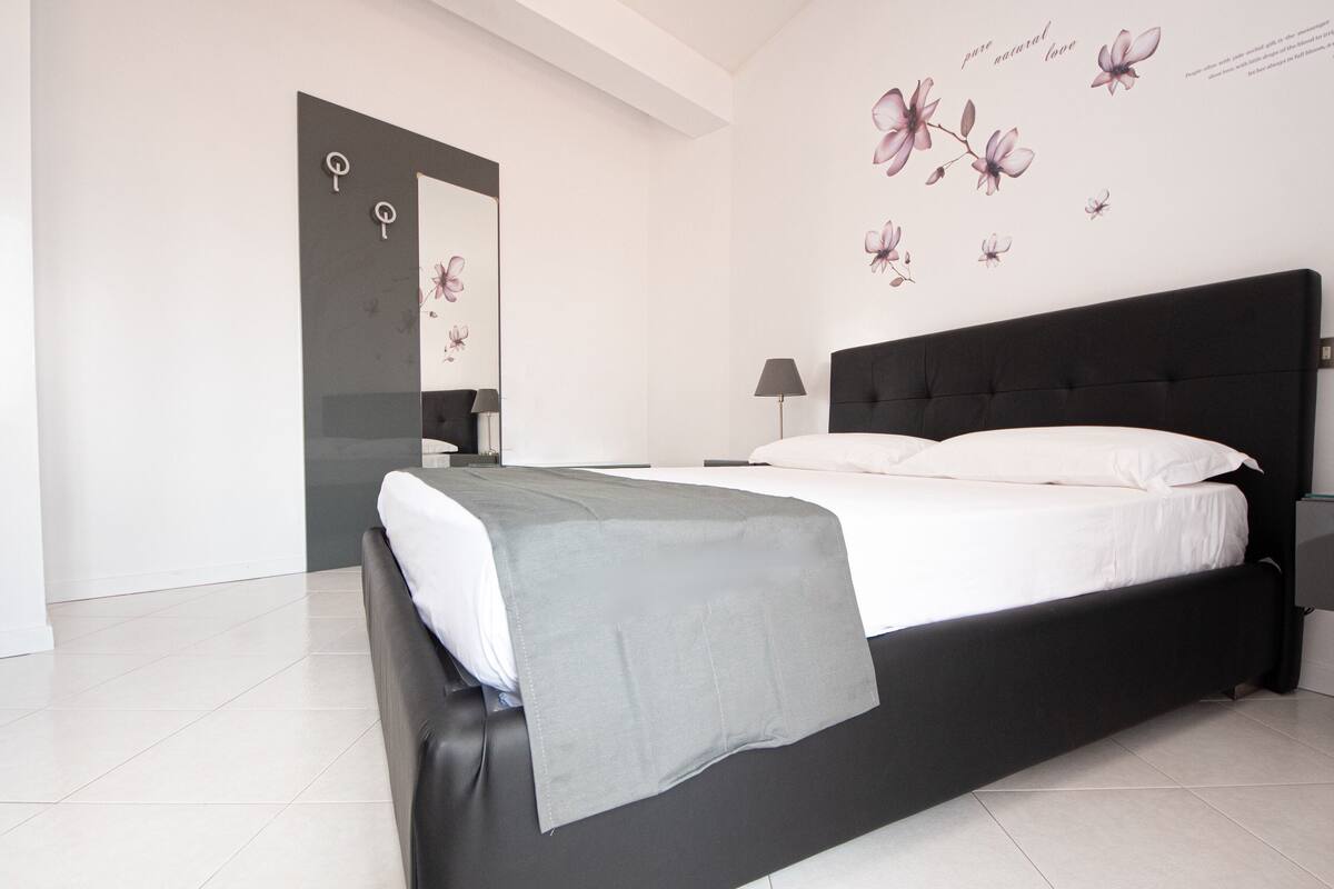 A modern bedroom with a black headboard, white bedding, and a grey throw blanket.