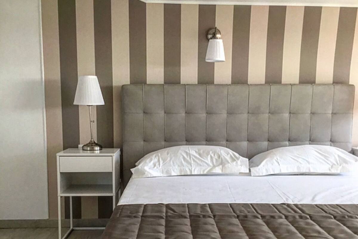 A neatly arranged bedroom with a large bed, a bedside table with a lamp, and a striped wall.
