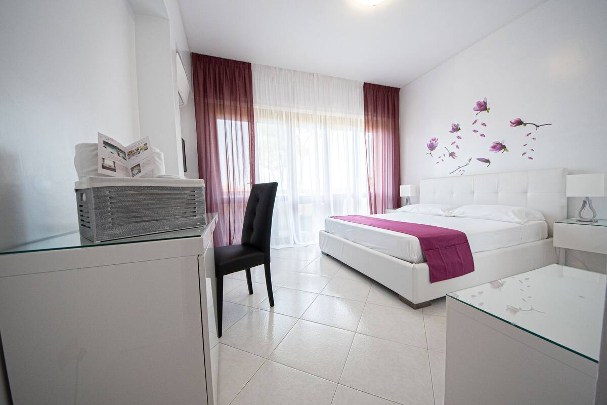 A hotel room with a bed, a chair, a desk, and a window with curtains.