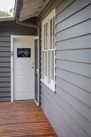 A house with a white door, a window with white shutters, and a wooden deck.