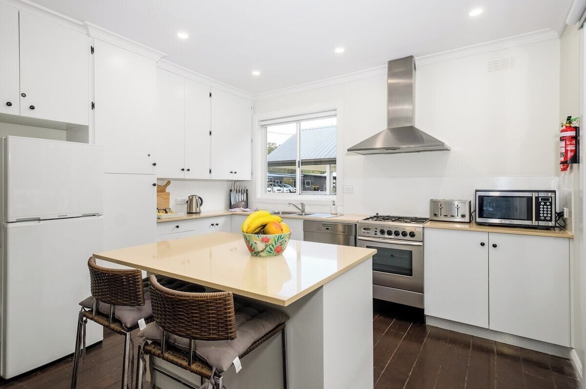 A modern kitchen with white cabinets, stainless steel appliances, a central island with seating, and a window providing natural light.