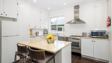 A modern kitchen with white cabinets, stainless steel appliances, a central island with seating, and a window providing natural light.