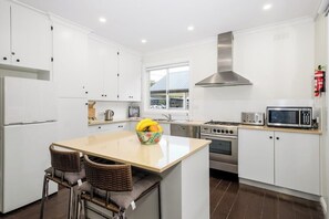 A modern kitchen with white cabinets, stainless steel appliances, a central island with seating, and a window providing natural light.