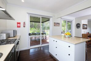 Une cuisine moderne dotée d’un grand îlot central, de portes-fenêtres coulissantes donnant sur une terrasse extérieure et offrant une vue sur le paysage.
