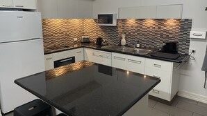 A modern kitchen with white cabinets, a black countertop, a microwave, a toaster, and a coffee maker. - Austral Place 88 over Merri River (Dennington)