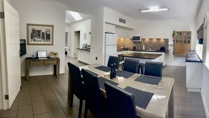 A modern kitchen with a microwave, refrigerator, and a tiled backsplash. There is a dining area with a table and chairs, and a small kitchen island. - Austral Place 88 over Merri River (Dennington)